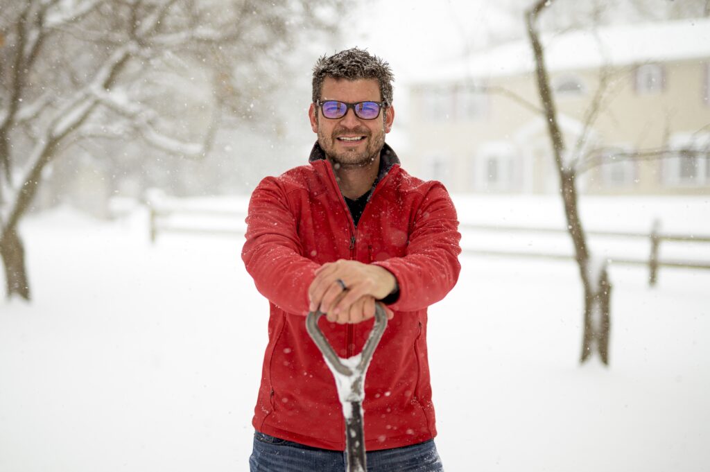 closeup shot of a male with his hands on the snow shovel and smiling towards the camera